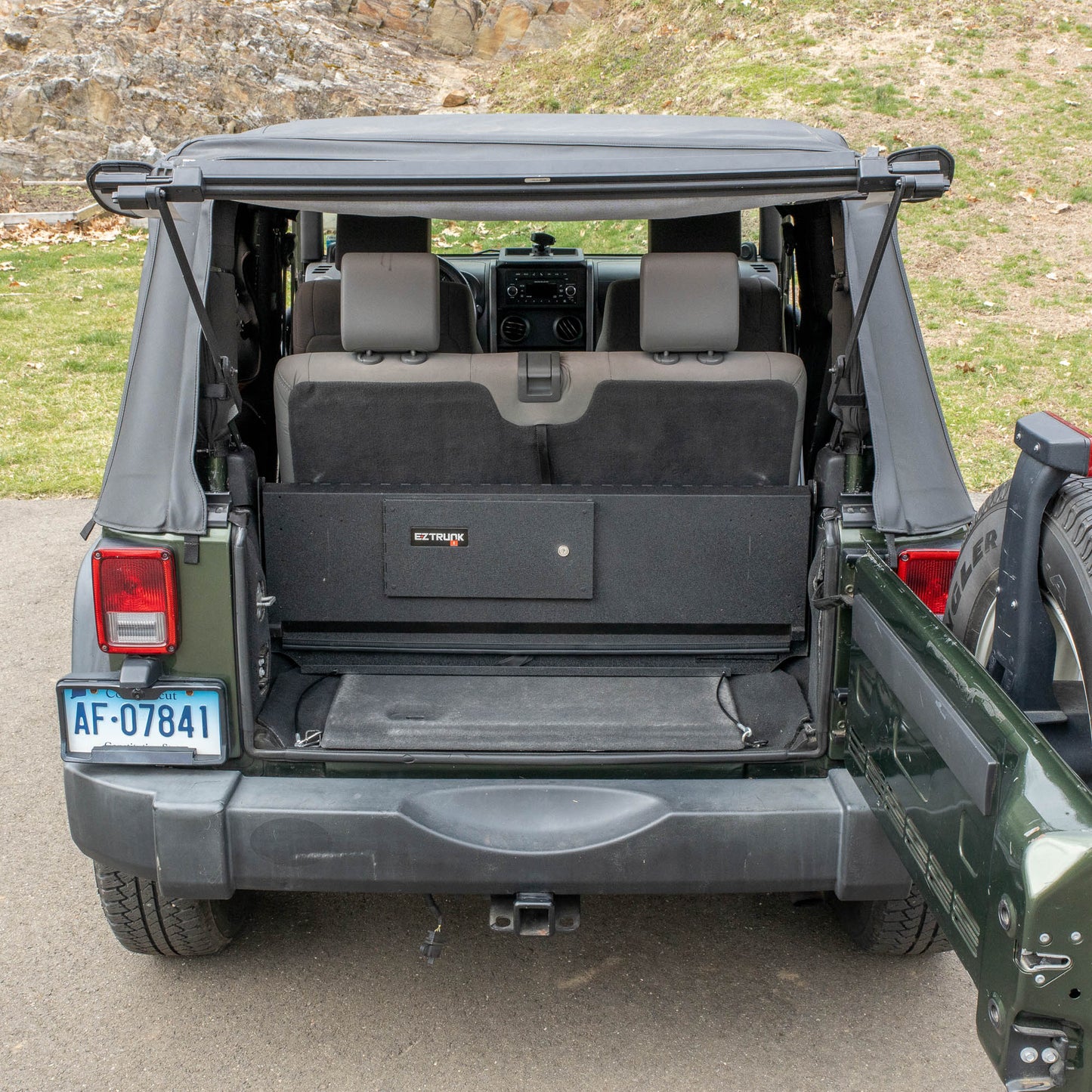 Straight-on view of black EZTrunk folded back in cargo area of green Jeep Wrangler with trunk door open.