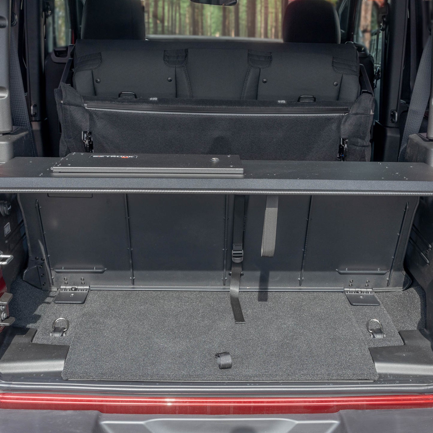 Straight-on view of black EZTrunk in cargo area of red Jeep Wrangler with trunk door open, showing secure storage setup.