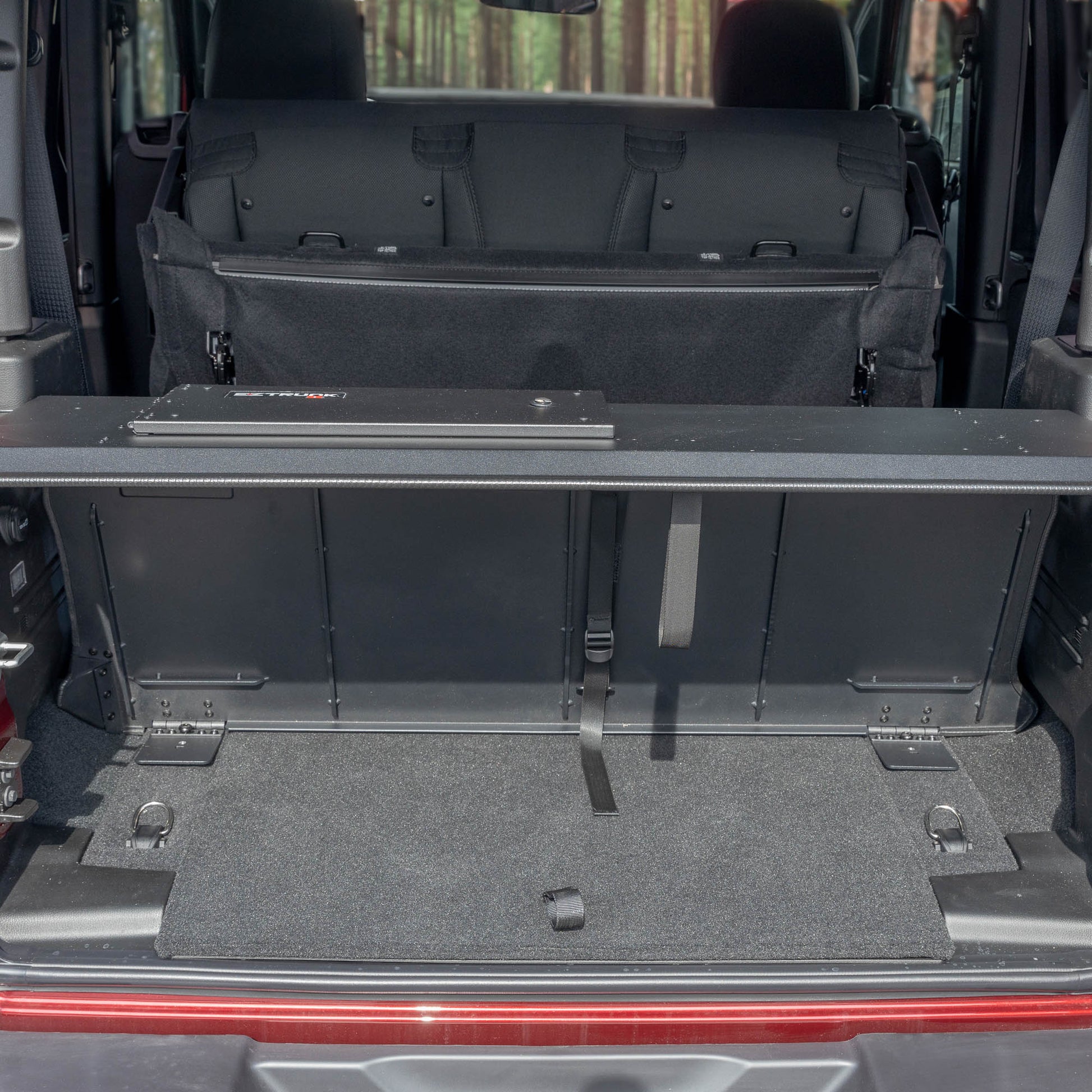 Straight-on view of black EZTrunk in cargo area of red Jeep Wrangler with trunk door open, showing secure storage setup.