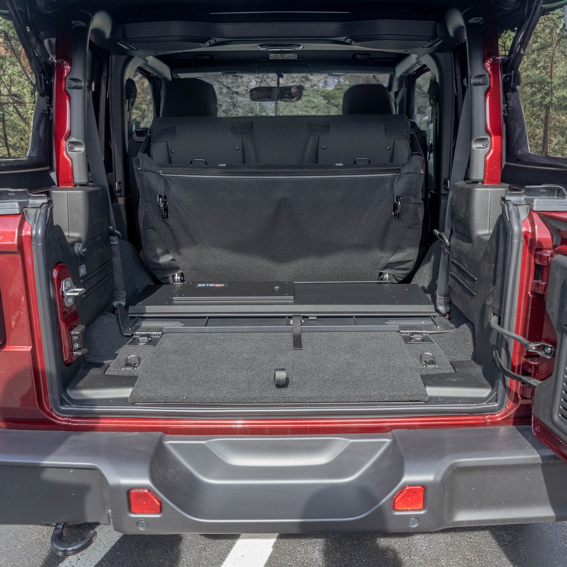 Straight-on view of black EZTrunk flattened in cargo area of red Jeep Wrangler with trunk door open, showing low-profile fit.