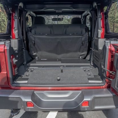 Straight-on view of black EZTrunk flattened in cargo area of red Jeep Wrangler with trunk door open, showing low-profile fit.