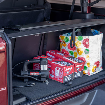 Side view of black EZTrunk installed with items inside cargo area of Jeep Wrangler with trunk door open, showing storage use.