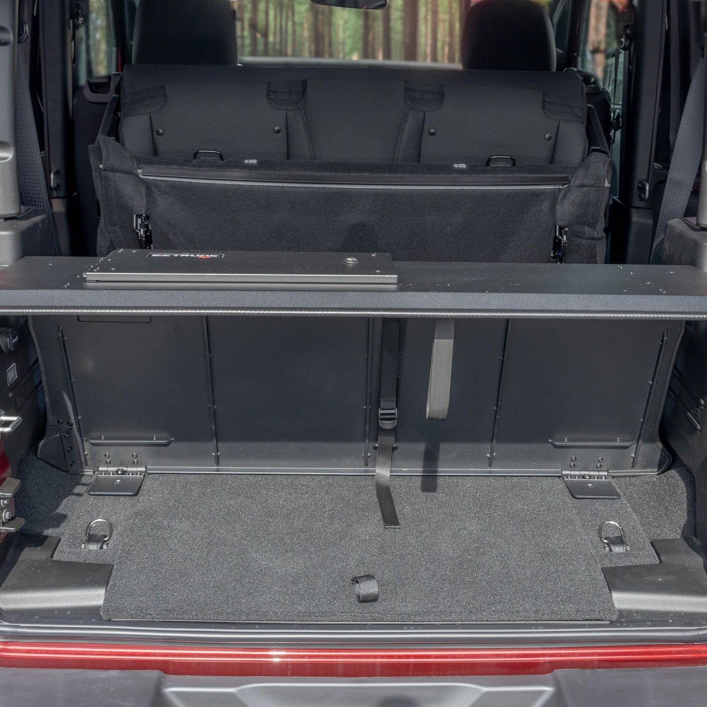 Straight-on view of black EZTrunk in cargo area of red Jeep Wrangler with trunk door open, showing secure storage setup.