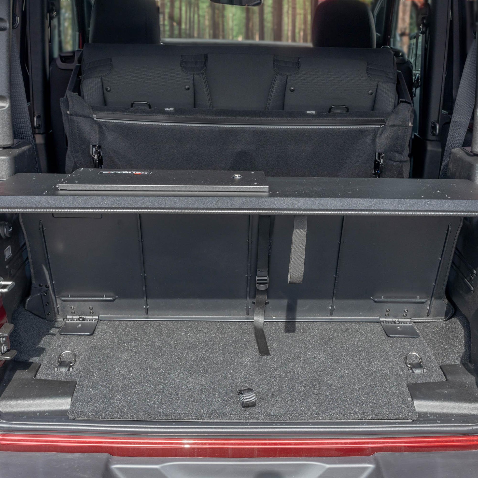 Straight-on view of black EZTrunk in cargo area of red Jeep Wrangler with trunk door open, showing secure storage setup.
