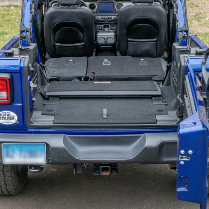 Black EZTrunk folded up in cargo area of blue Jeep Wrangler, showcasing compact, secure storage and space-saving design.