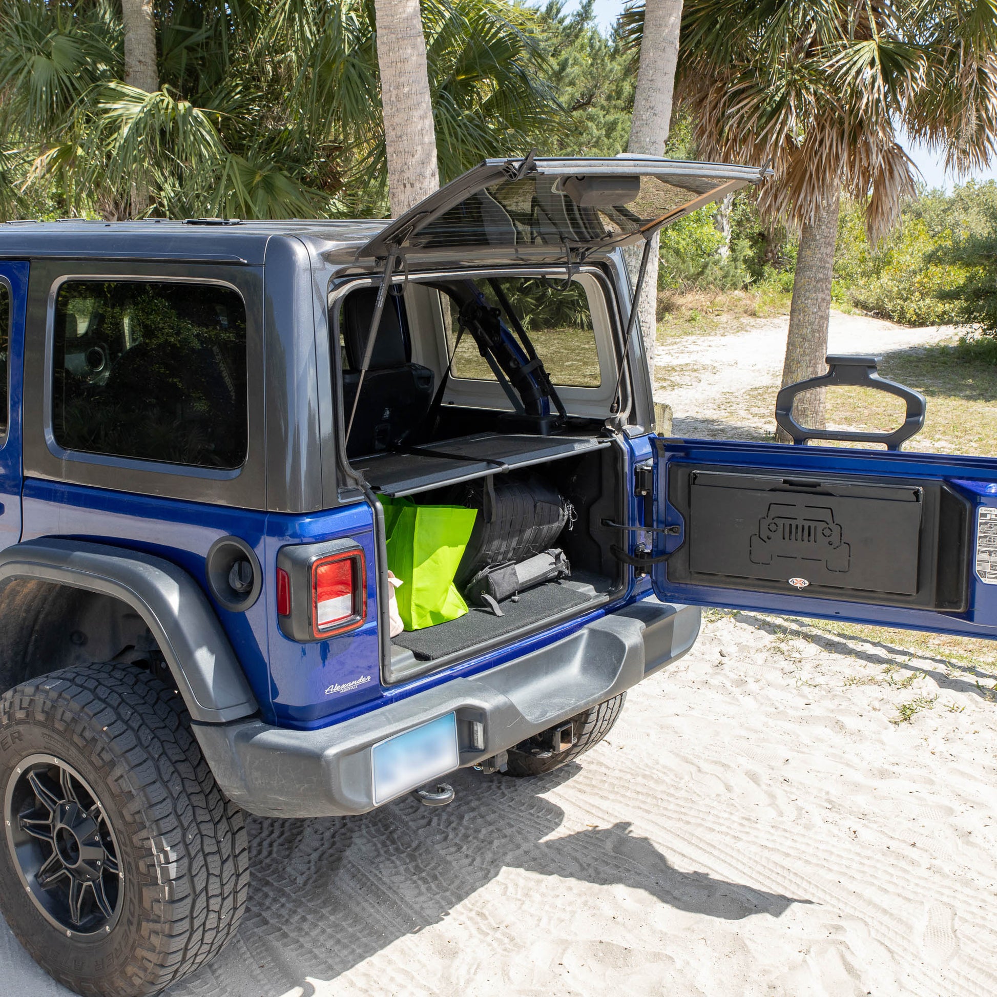 Black EZTrunk in blue Jeep Wrangler cargo area with gear inside and folded flat, shown with EZWindow and EZ Tailgate Table.