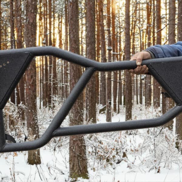 Person holding black Razor aluminum tube doors in snowy forest, showing lightweight, rugged off-road Jeep accessory.