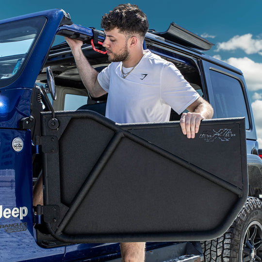Man in a white shirt entering a blue Jeep Wrangler equipped with EZ4X4 Phantom Tube Doors, all-weather panels, and round mirrors.