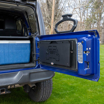 EZ4X4 Extreme Tailgate Table installed and folded up on a blue Jeep, highlighting its space-saving design for off-roading and camping.