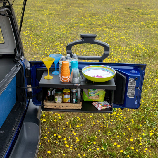 Front view of black foldable tailgate table mounted on Jeep, shown holding food and drinks—perfect for camping and tailgating.