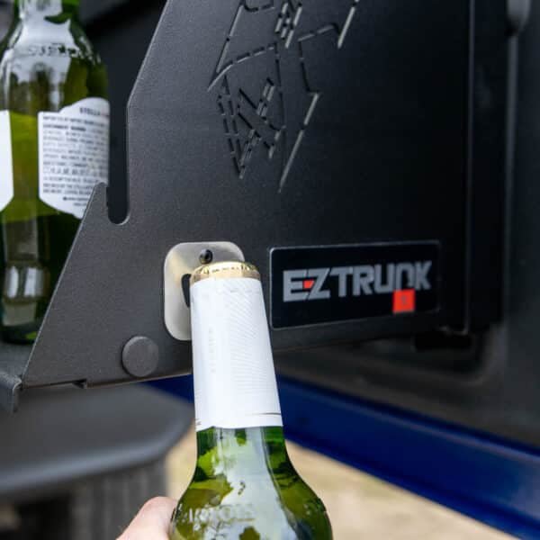 Person using built-in bottle opener on black Jeep tailgate table to open champagne—highlighting off-road convenience.