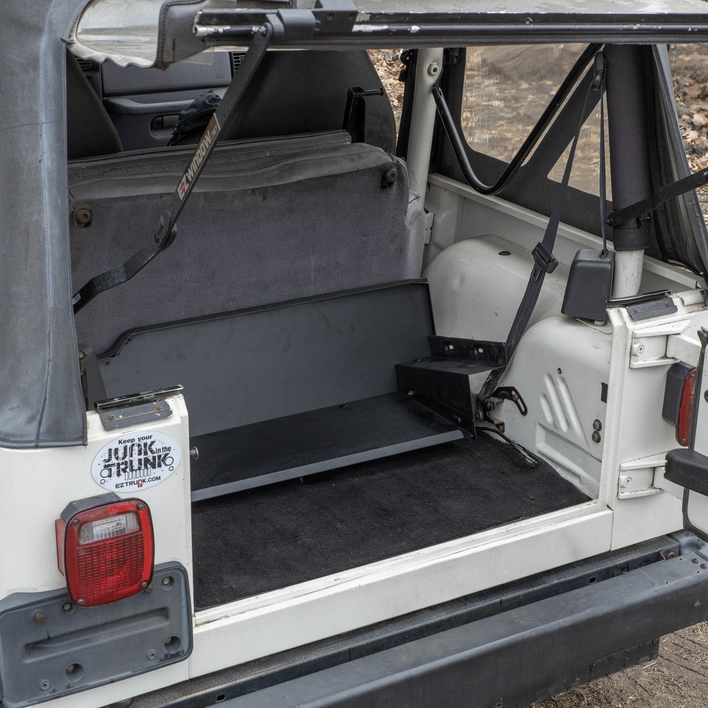 Black EZTrunk shown completely flat in cargo area of white Jeep TJ with trunk door open, highlighting low-profile fit.