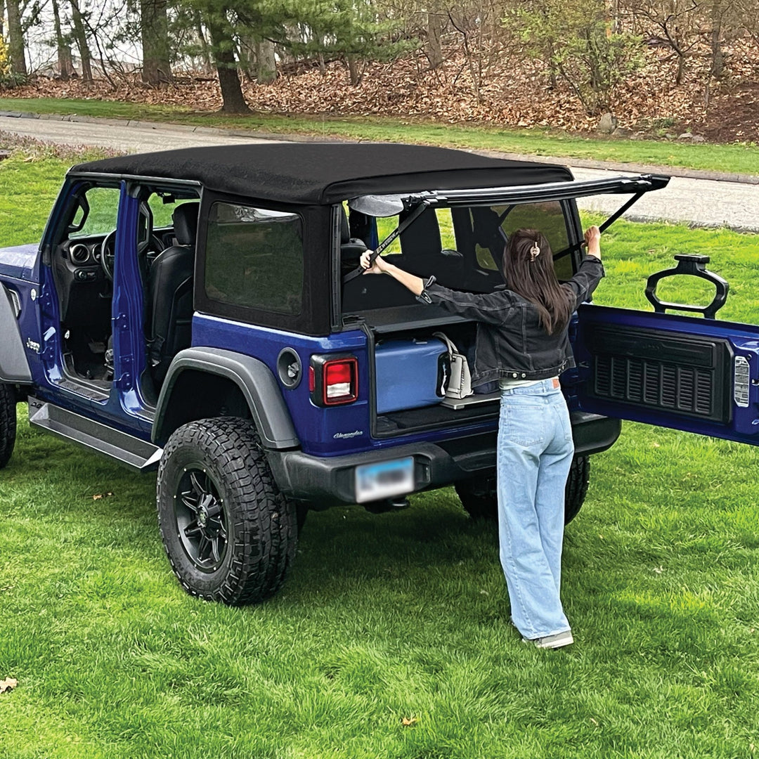 Woman setting up EZWindow in rear of blue Jeep Wrangler, showing easy install and improved ventilation for off-road trips.