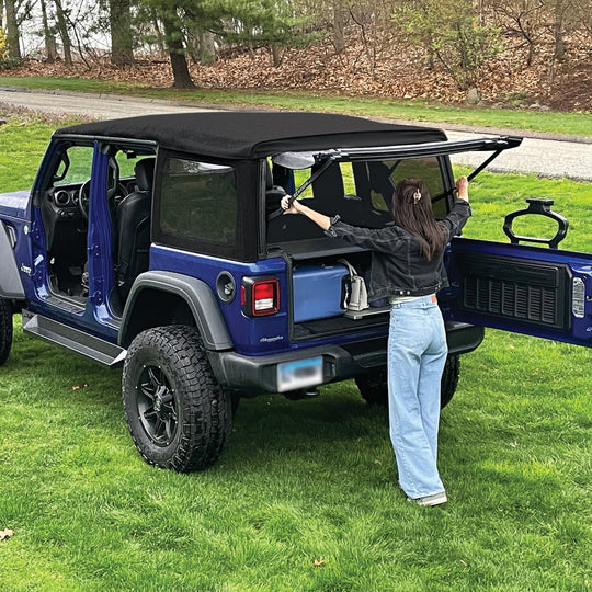 Woman setting up EZWindow in rear of blue Jeep Wrangler, showing easy install and improved ventilation for off-road trips.