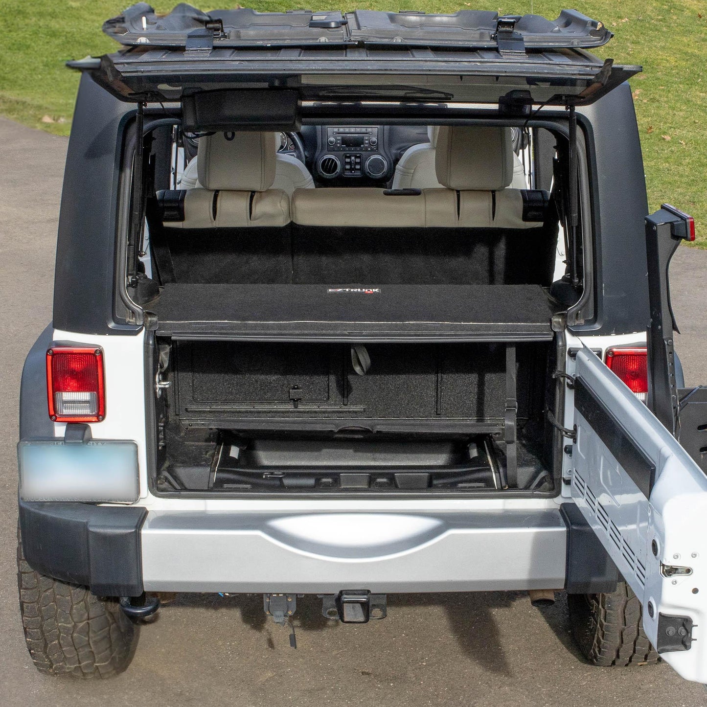 Straight-on view of black EZTrunk in cargo area of white Jeep Wrangler with trunk door open, showing secure storage setup.