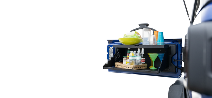 Black EZ4X4 Extreme Tailgate Table mounted on a Jeep, holding food and drinks for camping or tailgating.