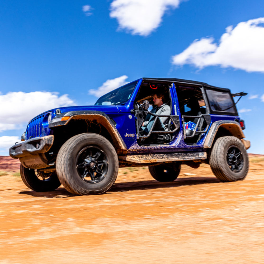 Person driving a muddy blue 4-door Jeep Wrangler with EZ4X4 Razor Tube Doors on a red dirt desert trail.