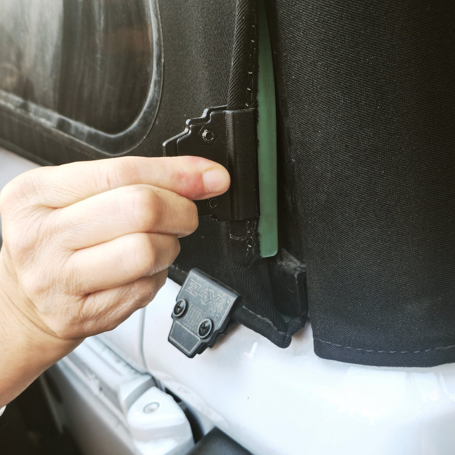 Person installing an aftermarket soft top clip on a Jeep Wrangler, showing secure attachment of the soft top.