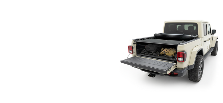A tan Jeep Gladiator with the tailgate down, revealing gear secured in the truck bed by an EZ4X4 cargo management system under a partially open tonneau cover.