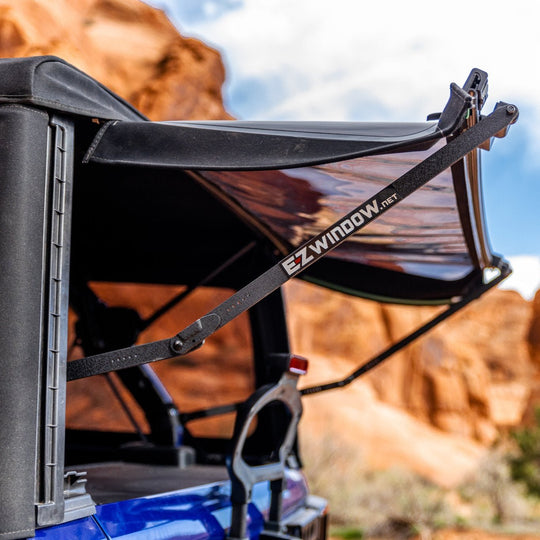 Black EZWINDOW open on blue Jeep, allowing clear visibility into cargo area while providing shade and ventilation.