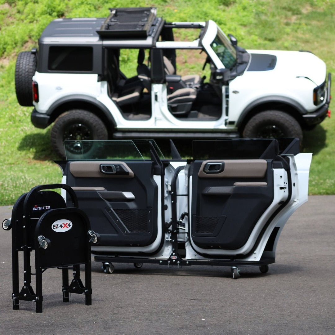 White Ford Bronco with all four doors on EZ4X4 door carts; second cart compacted for easy transport on driveway.