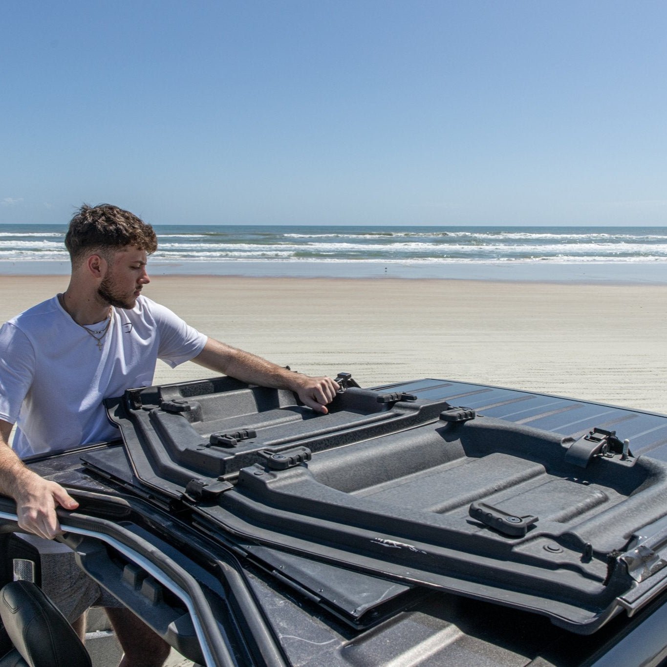 Man at beach with Freedom Panels flipped up on Jeep roof using EZ FlipTop hinges, showcasing easy, one-person off-road setup.
